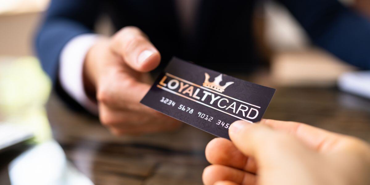 An employee hands a customer a business loyalty card as part of their brand loyalty strategy for retaining customers.